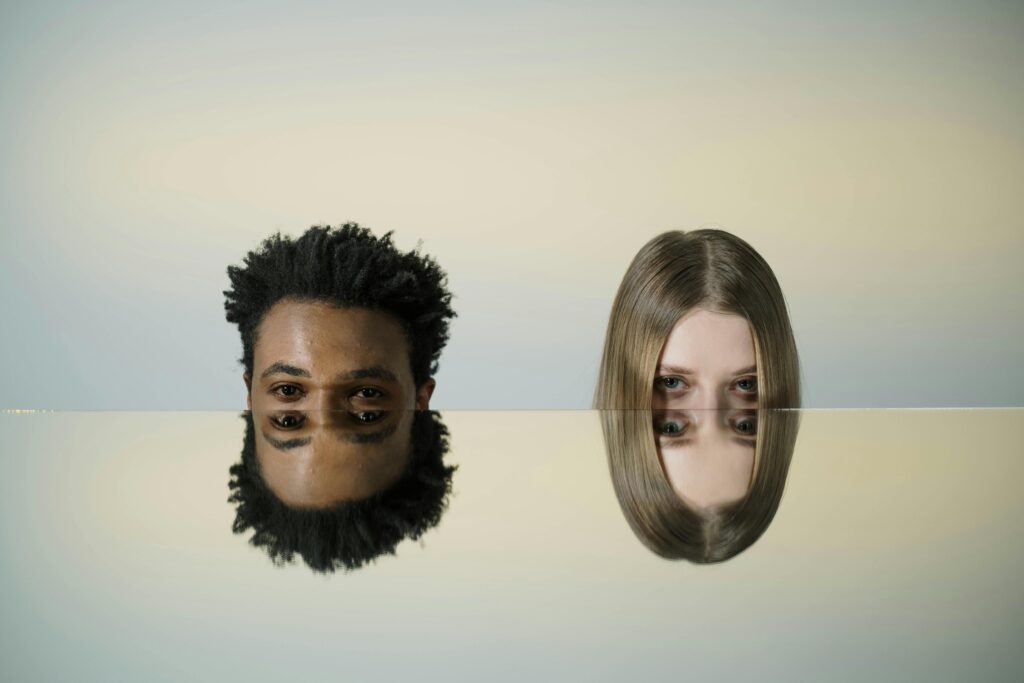 Two faces mirrored on a smooth surface creating a dual reflection effect.