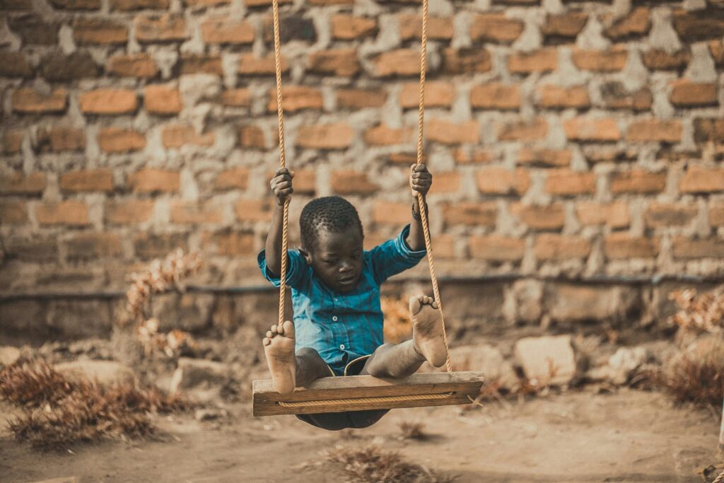 pexels-photo-1686467-1686467 A young boy enjoys a playful moment swinging outdoors in front of a rustic brick wall.